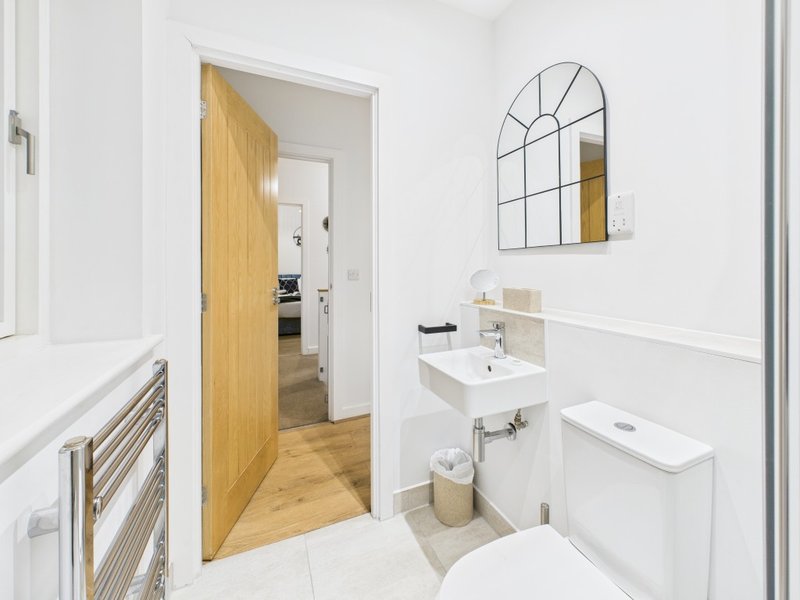Modern bathroom with white walls, wall-mounted sink, toilet, and arched mirror
