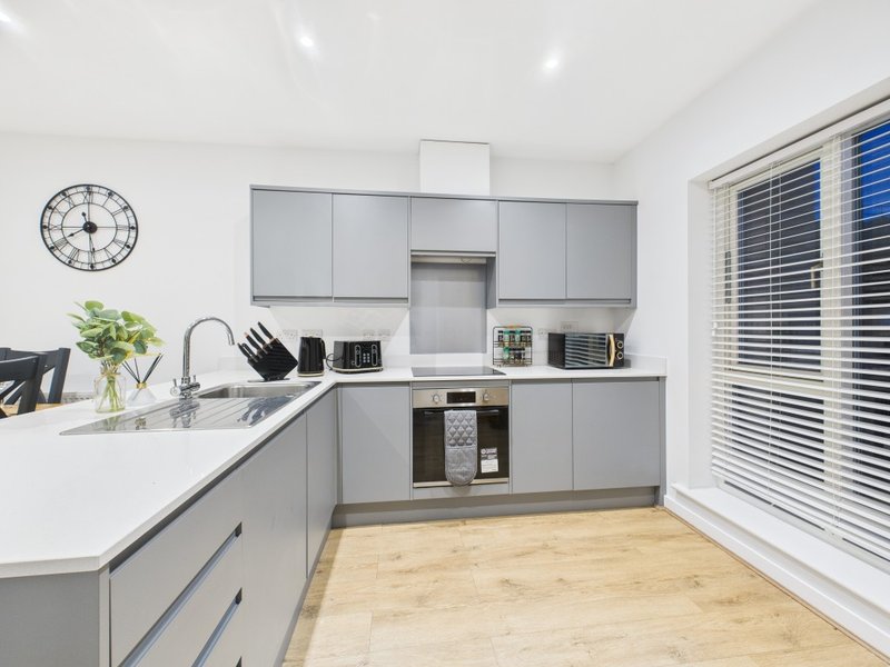 Modern kitchen with gray cabinetry, white countertop, wooden flooring and wall clock