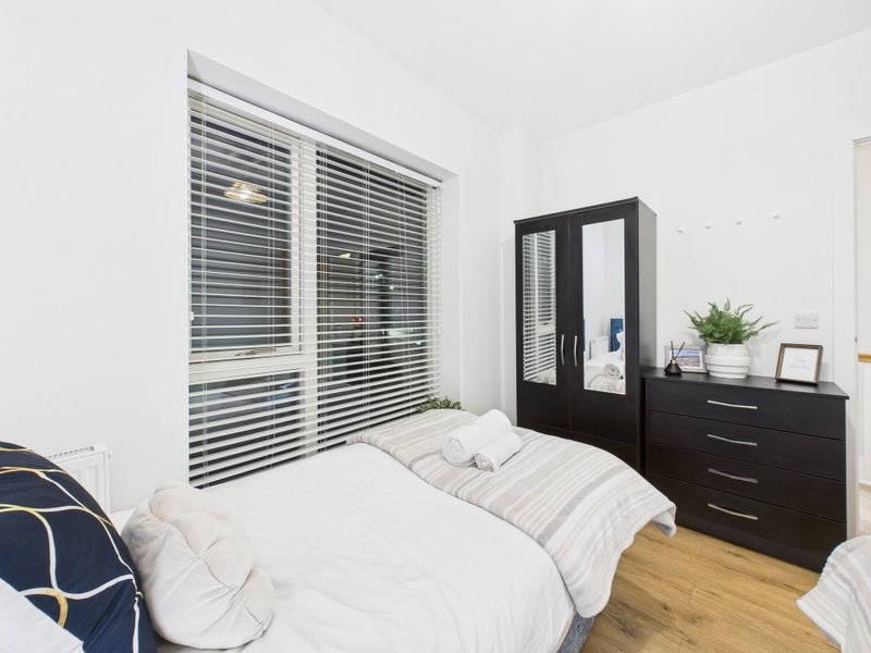Modern bedroom with double bed, black wardrobe, wooden floor and louvered window blinds