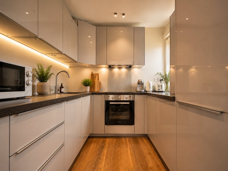 Modern kitchen with white cabinetry, black countertops, wooden flooring, and integrated appliances.