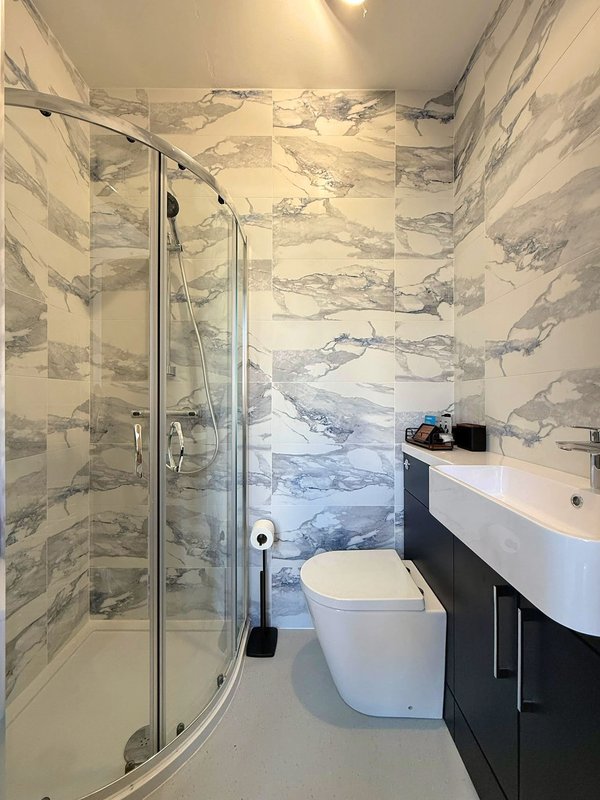 Modern bathroom with marble tiling, curved shower enclosure, white toilet and black vanity sink