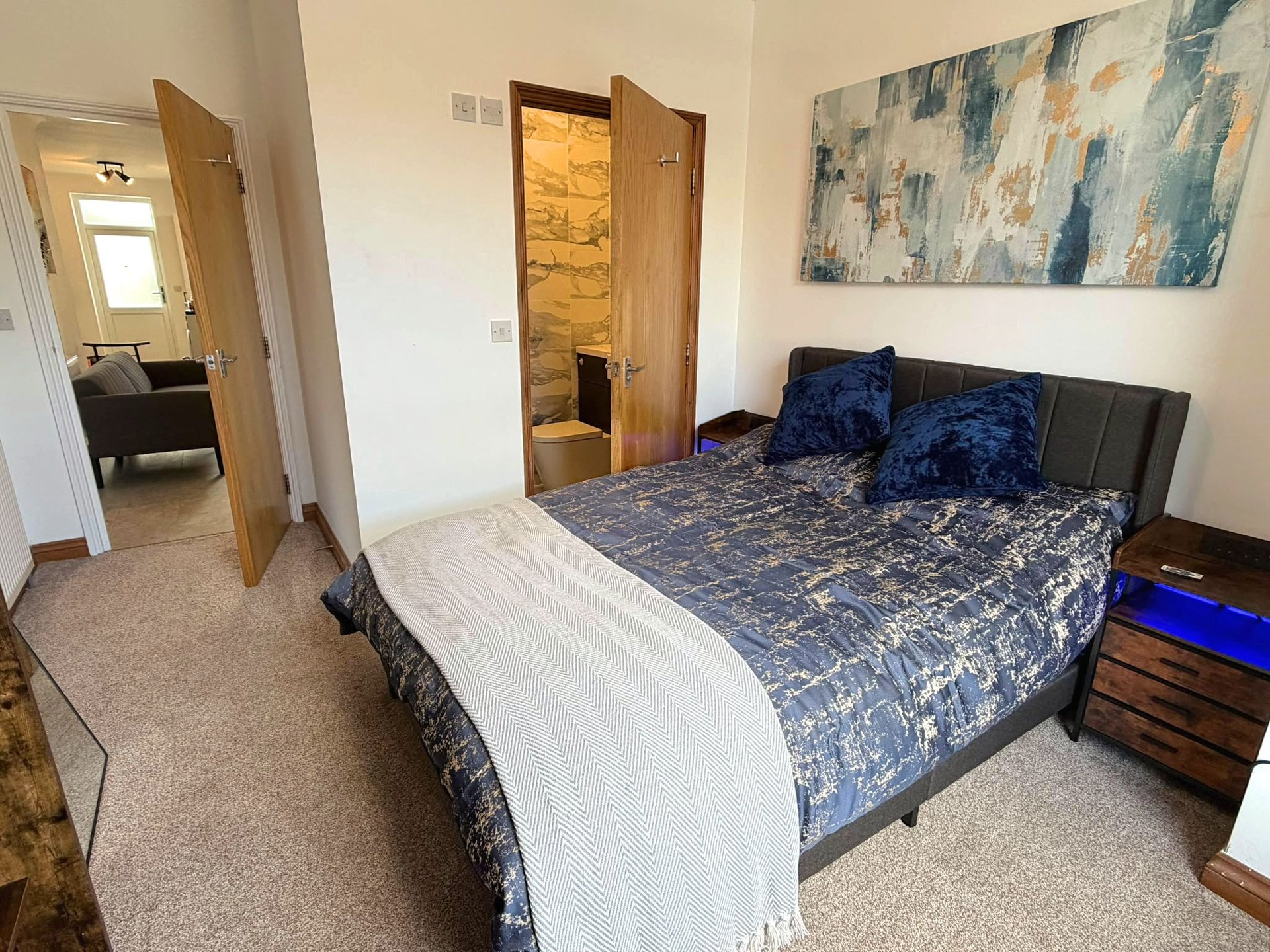Bedroom with double bed, blue patterned bedding, wooden nightstand, and open doorways