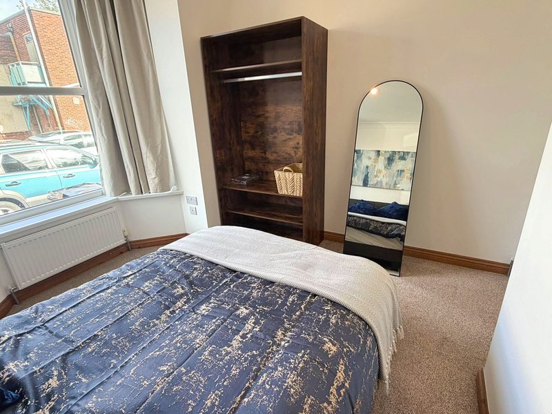 Bedroom with double bed, dark wooden wardrobe, mirror, and window with radiator