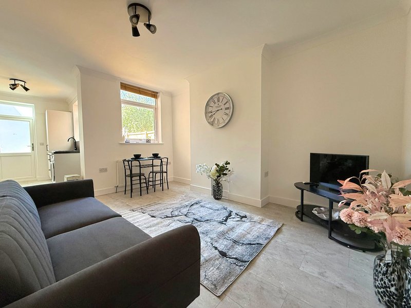 Modern living room with grey sofa, dining area, wall clock, TV and flowers
