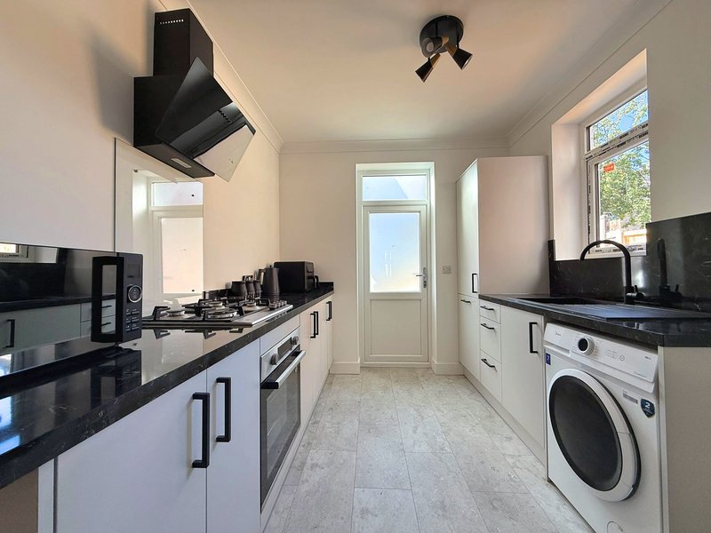 Modern kitchen with white cabinetry, black countertops, stainless steel appliances and washing machine
