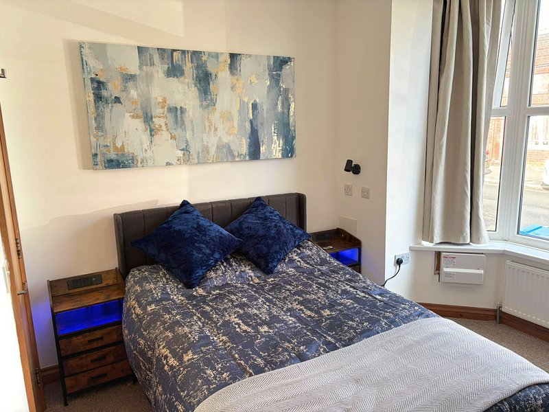 Modern bedroom with double bed, blue cushions, abstract wall art and large window