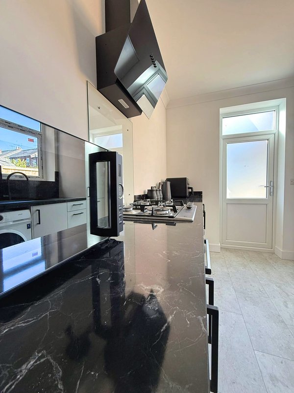 Modern kitchen with black marble countertop, built-in appliances, and door to garden