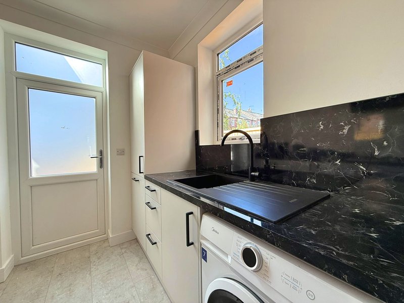 Modern kitchen with white cabinetry, black marble countertop, white door and windows