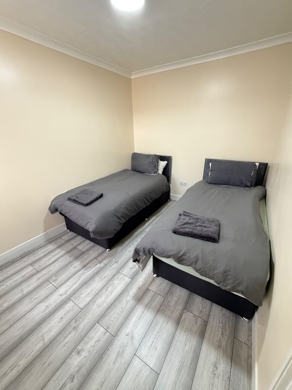 Bedroom with two single beds, grey bedding, wooden floor and cream walls