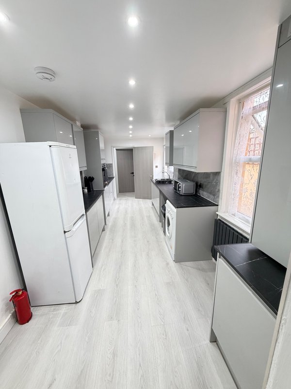 Modern galley kitchen with white appliances, light wood flooring, recessed ceiling lights