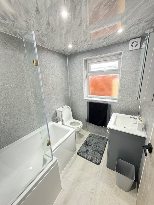 Modern bathroom with white bathtub, glass shower screen, toilet, sink and window