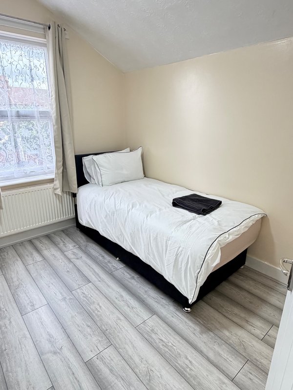 Single bedroom with white bedding, wooden floor, window with curtains and radiator