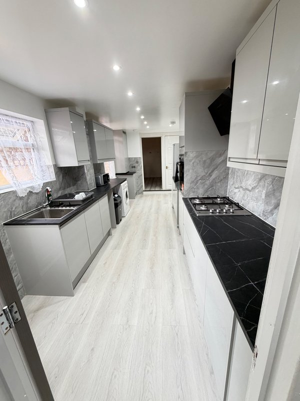 Modern galley kitchen with white cabinetry, marble splashback, black countertops and appliances