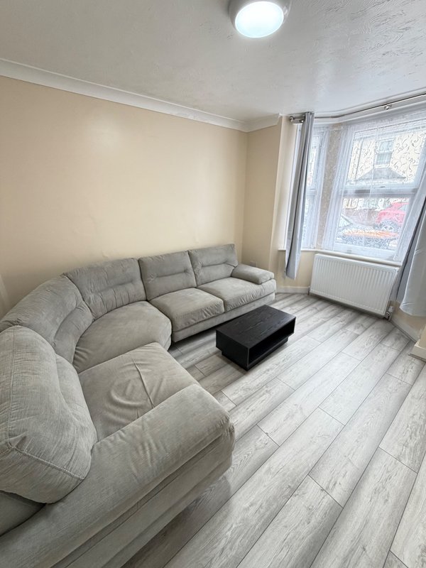 Modern living room with grey curved sofa, black coffee table, wooden flooring and large window