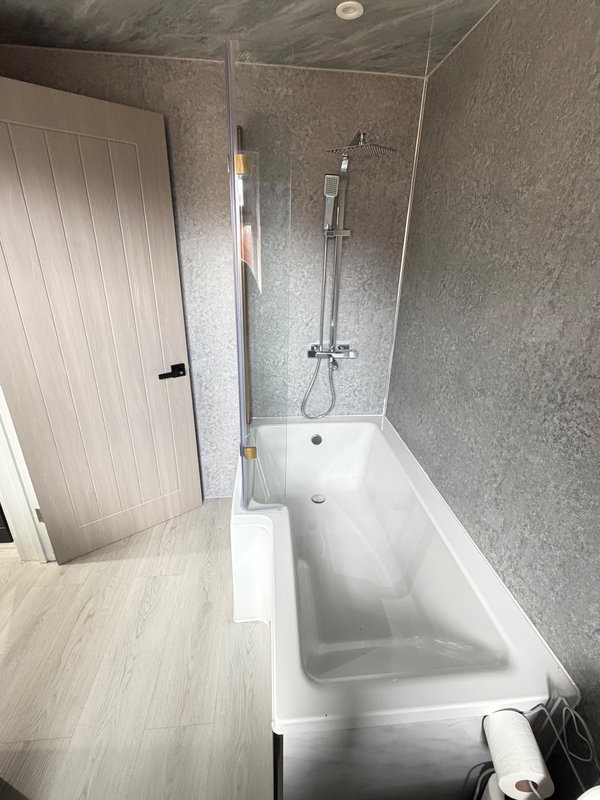 Modern bathroom with white bathtub, glass shower screen, grey tile walls and wooden flooring