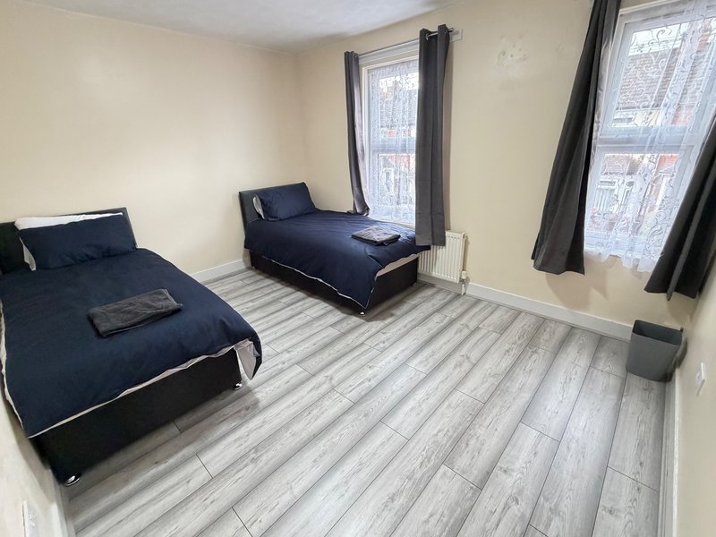 Shared bedroom with two single beds, grey wood-effect flooring, and windows with dark curtains