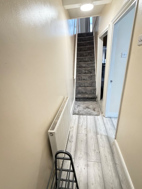 Narrow hallway with stairs, radiator, light flooring and cream walls