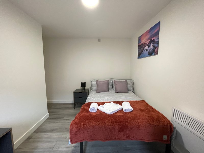 Compact bedroom with double bed, rust-coloured throw, white towels, and landscape wall art