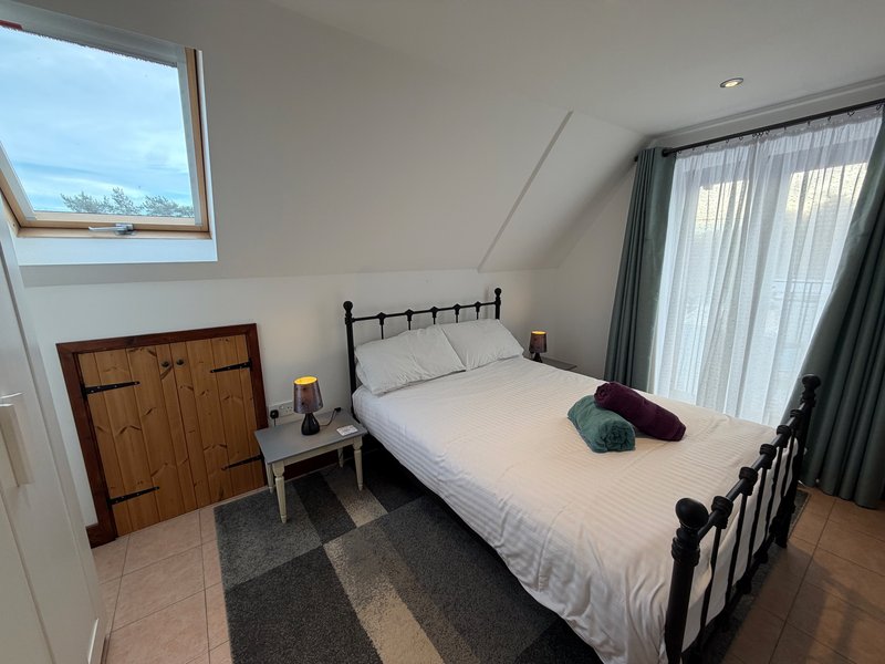 Bright attic bedroom with double bed, wooden wardrobe, skylight window and curtains