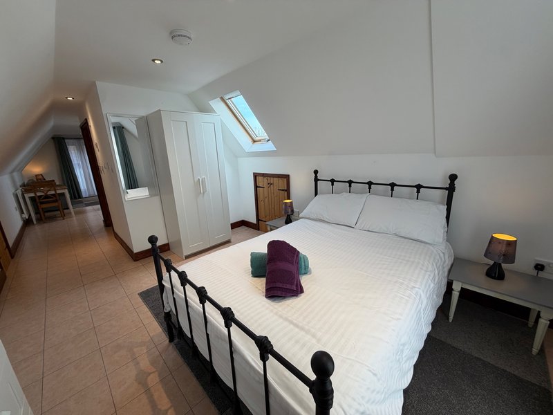 Bright attic bedroom with double bed, metal frame, white bedding, and sloped ceiling with skylight