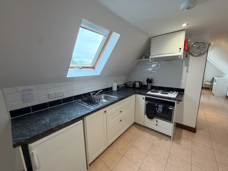 Small kitchen with cream cabinets, black countertop, skylight window and appliances