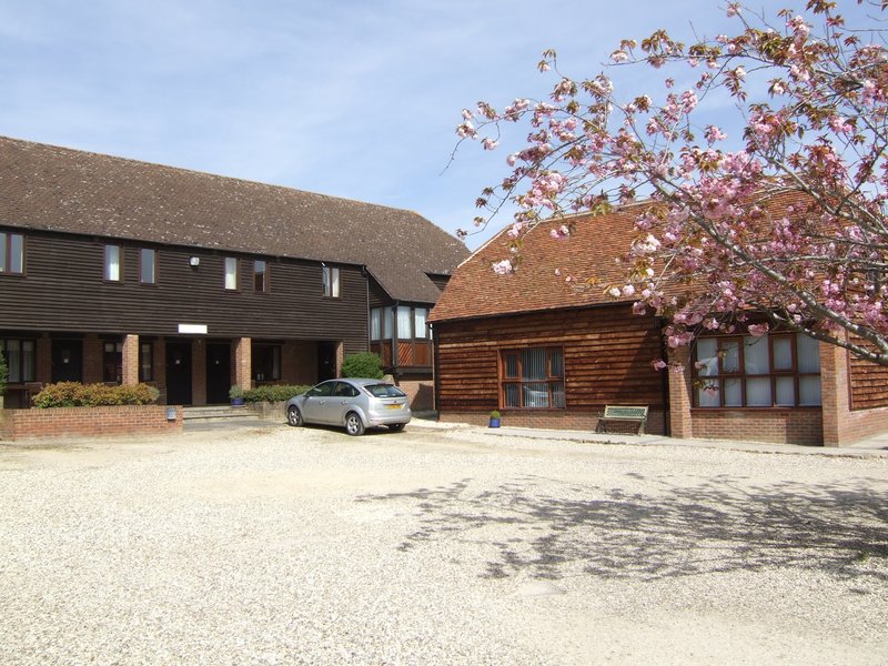 Converted barn properties with gravel courtyard, parked car, and blooming cherry tree