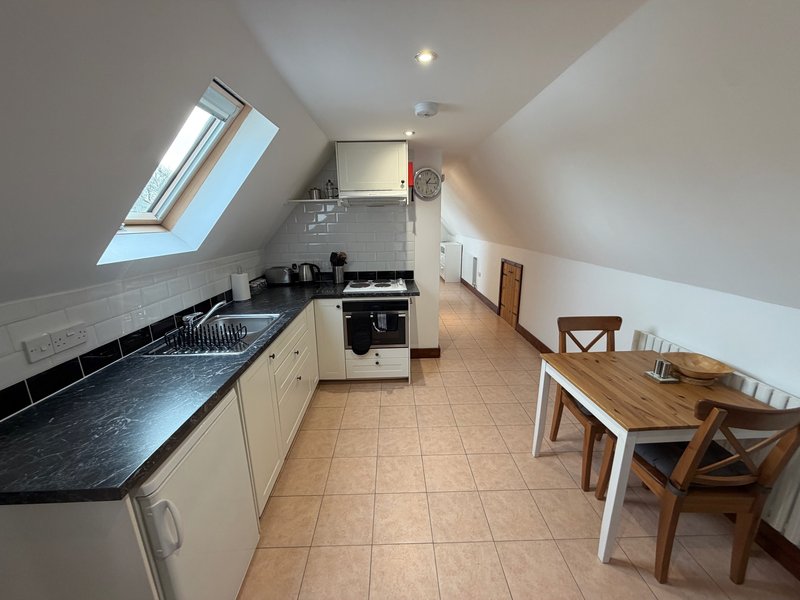Attic kitchen with cream cabinets, black countertops, wooden dining table and skylight