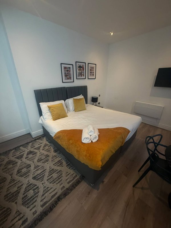 Modern bedroom with double bed, gold throw, white pillows and framed wall art above headboard