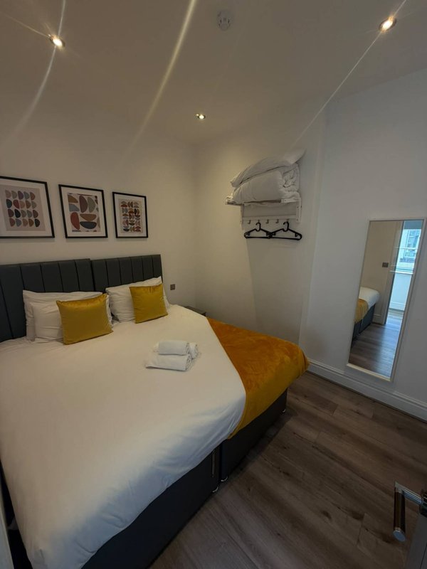 Modern bedroom with double bed, yellow cushions, framed wall art, and wooden flooring