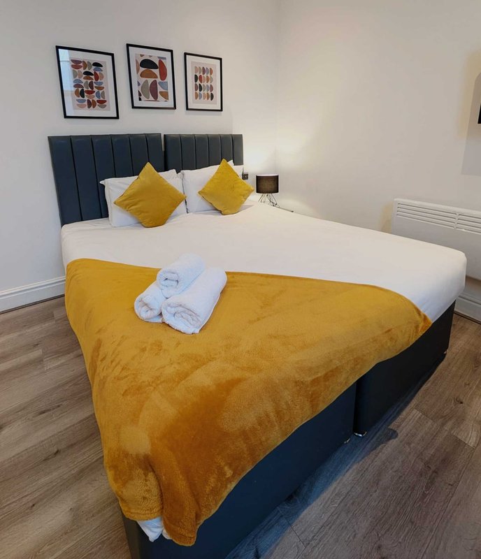 Modern bedroom with double bed, yellow and white bedding, navy headboard, framed wall art