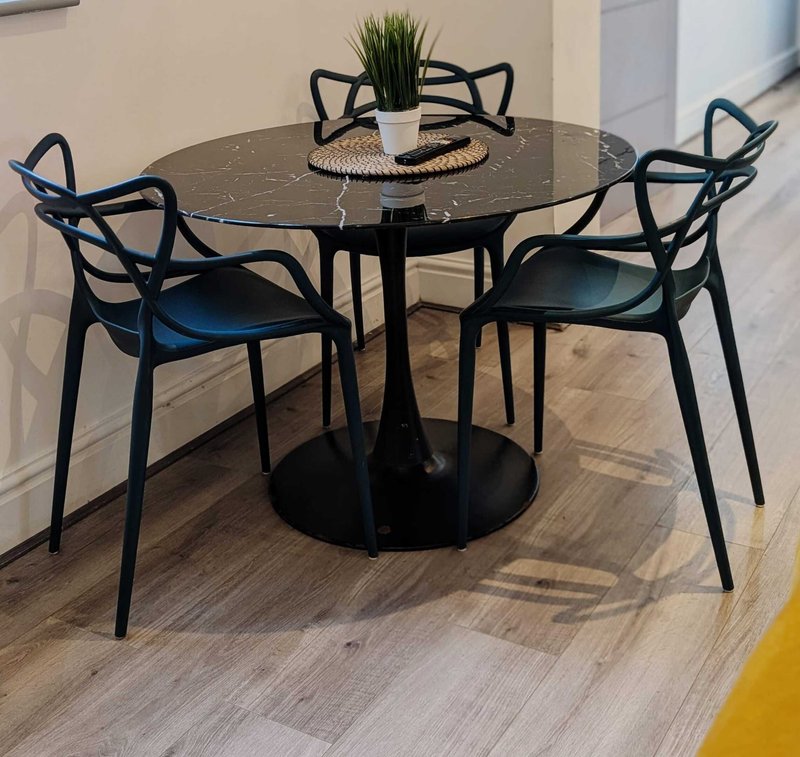Modern dining area with black round marble table, four black chairs with blue cushions, and potted plant centerpiece