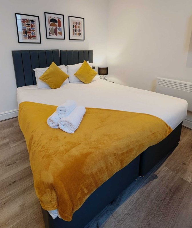 Modern bedroom with king bed, yellow bedding, black headboard, and framed wall art