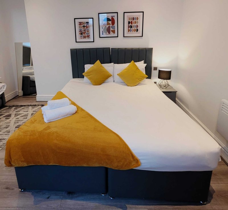 Modern bedroom with double bed, yellow cushions, dark headboard and framed wall art