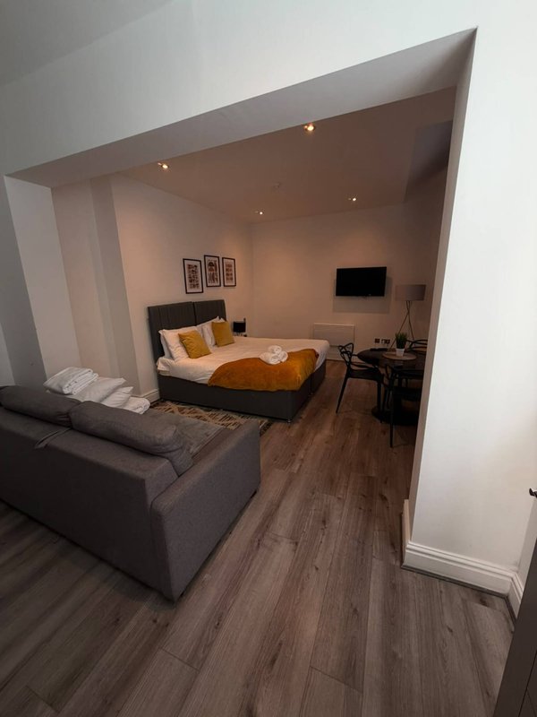 Modern studio bedroom with double bed, sofa seating, desk area and wall-mounted TV