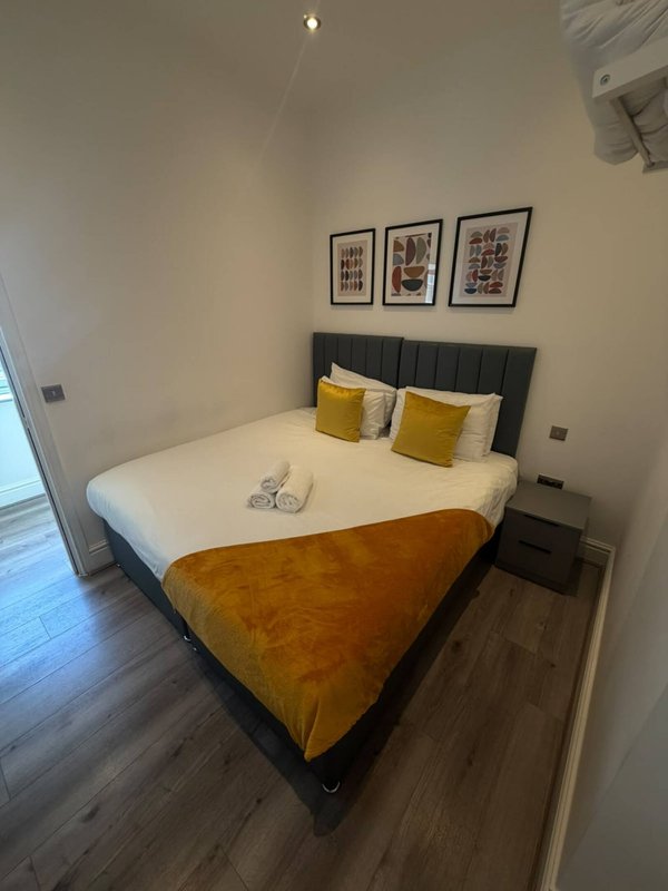 Modern bedroom with double bed, yellow and white cushions, framed wall art and wooden flooring