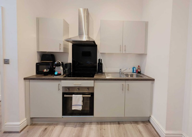 Modern compact kitchen with white cabinetry, black range cooker, stainless steel extractor hood and wooden countertop
