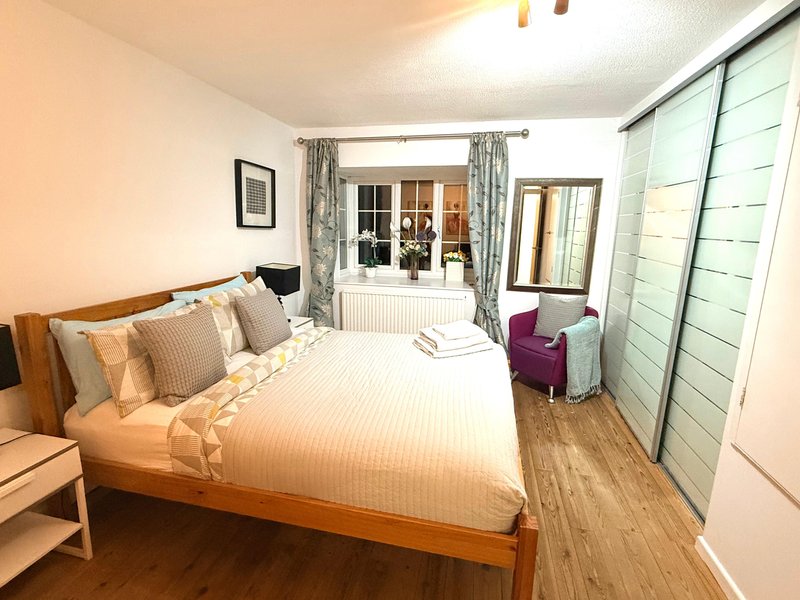 Spacious bedroom with king size bed, striped bedding, cushions, wooden floor and built-in wardrobes