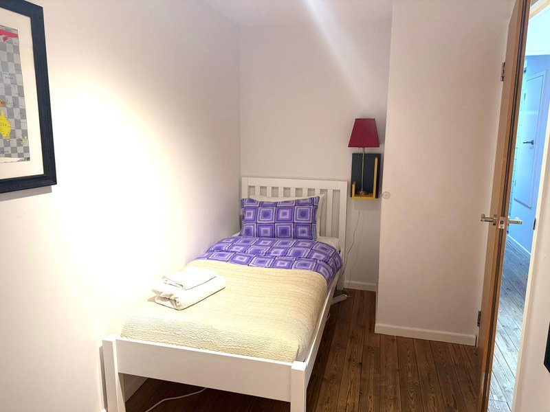 Small bedroom with single bed, purple bedding, wooden floor and wall art