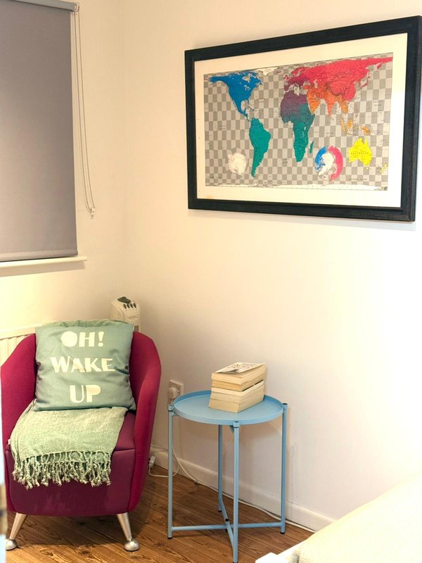 Bedroom corner with burgundy armchair, decorative cushion, small blue side table, and framed world map artwork