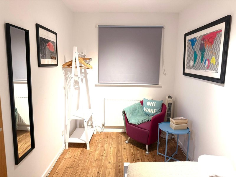 Compact bedroom with wooden floor, chair, small table, framed wall art and window