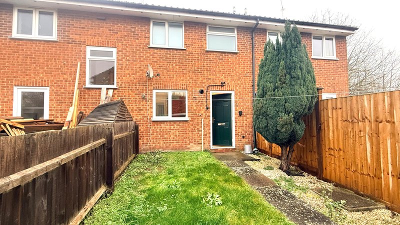 Rear of house with green door, small garden, wooden fencing.