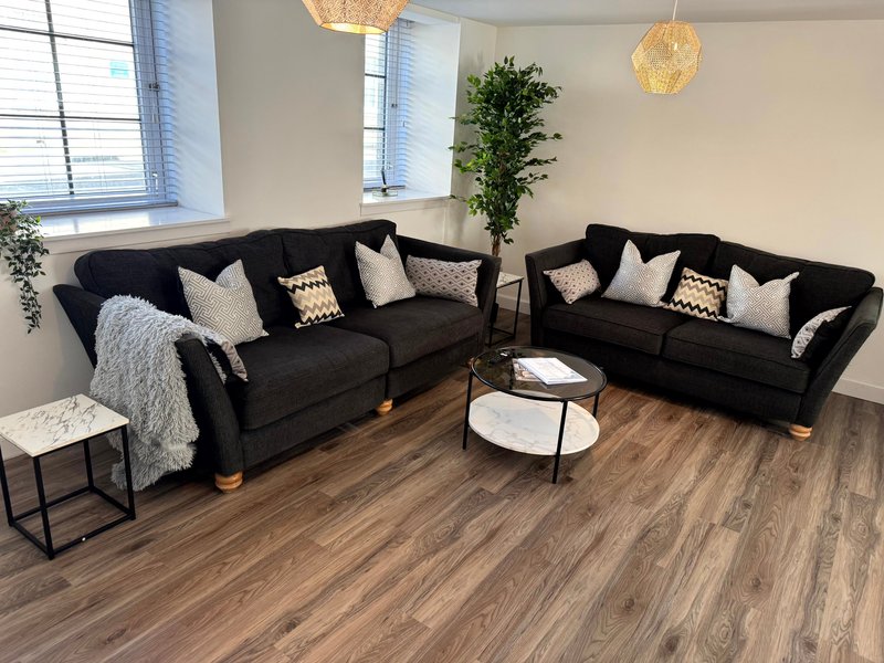 Spacious living room with two black corner sofas, wooden flooring, pendant lighting and potted plants