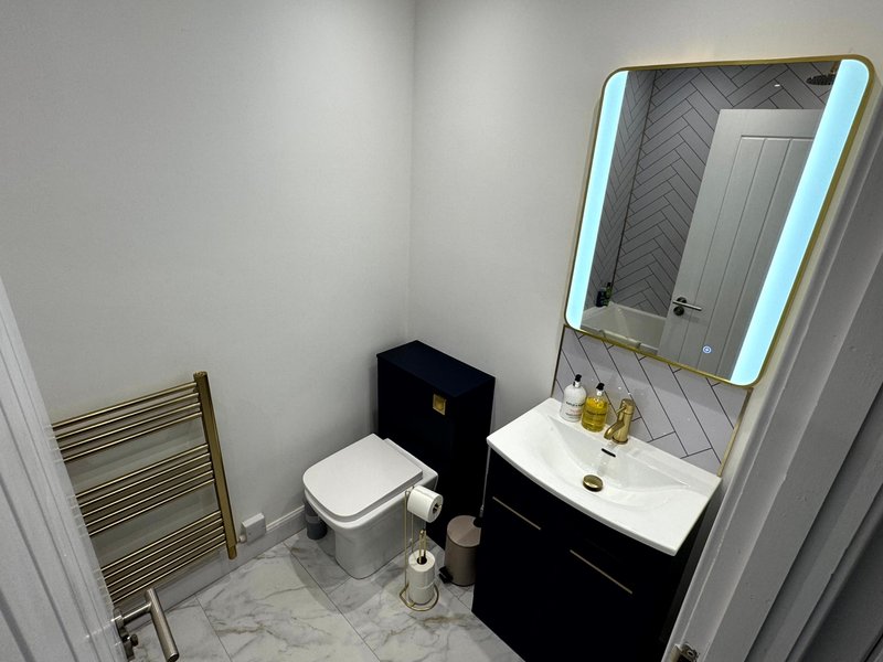 Modern bathroom with black vanity, white sink, illuminated mirror and heated towel rail