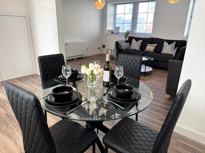 Modern dining room with round glass table, black quilted chairs, and black sofa seating area