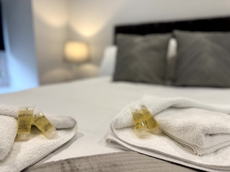 Bedroom with neatly folded towels and toiletries on bed, dark headboard visible