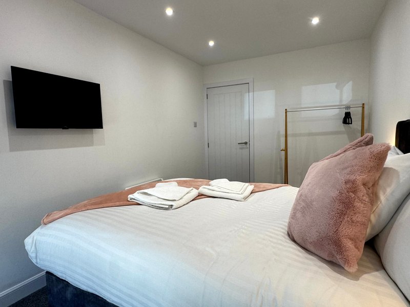 Modern bedroom with double bed, pink cushion, wall-mounted TV and ensuite door