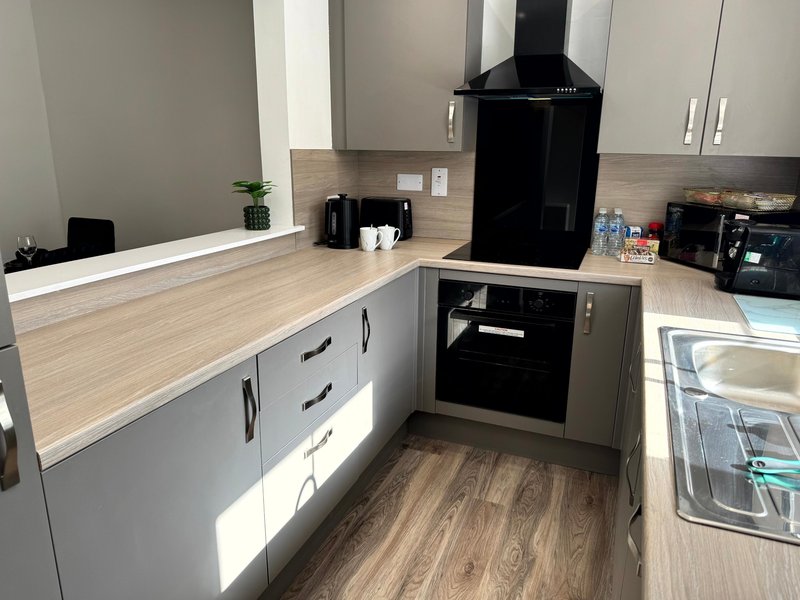 Modern kitchen with white cabinetry, wooden countertop, black range hood and built-in oven