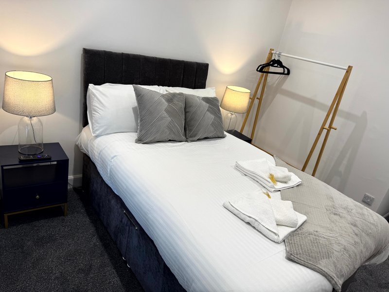 Modern bedroom with double bed, black headboard, grey pillows, bedside lamps and wooden clothing rack