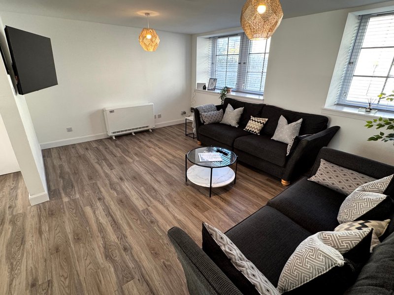 Modern living room with black sofas, wooden flooring, pendant lights and wall-mounted TV