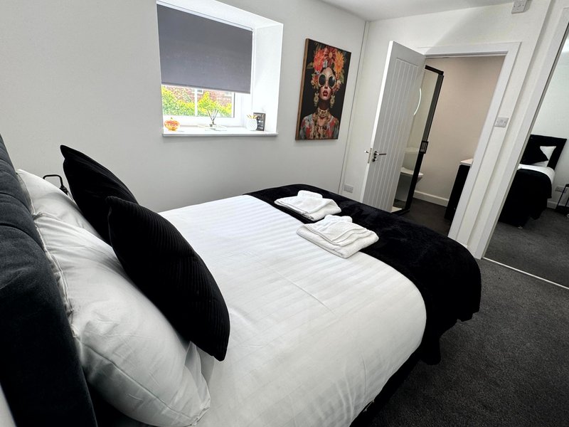 Modern bedroom with double bed, black cushions, white bedding, window with blind and wall art